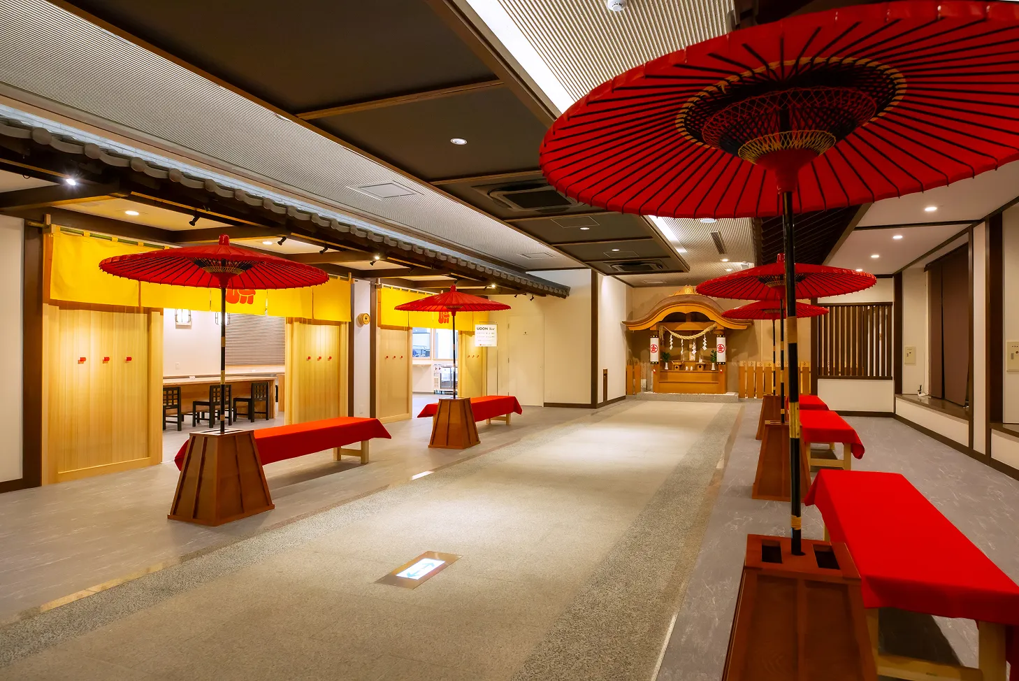ロビー。参道に見立てた中央の通路の両脇に、赤い毛氈が敷かれた長椅子と、番傘風の大きな赤い和傘（野点傘）が複数並んでいる。