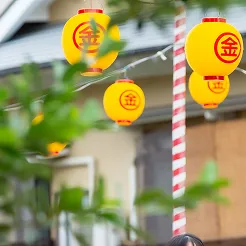 多数の黄色い丸型の提灯が、ひもやワイヤーに吊るされて並んでおり、提灯の中央には朱色で『金』の一文字が書かれています。