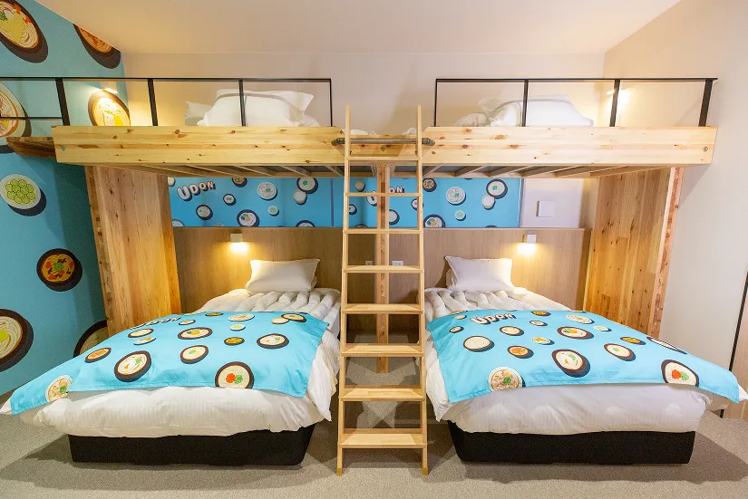 「UDONコンセプトルーム」ポップなうどん模様のベッドシートが敷いてあるツインベッドとロフト。